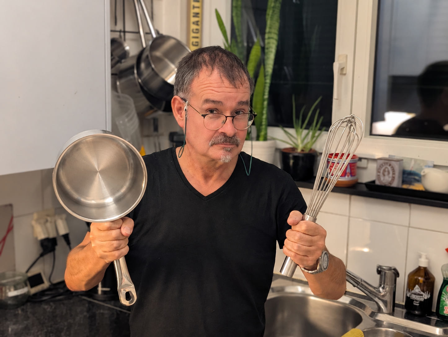 Sven in the kitchen with a frying pan and a large whisk.